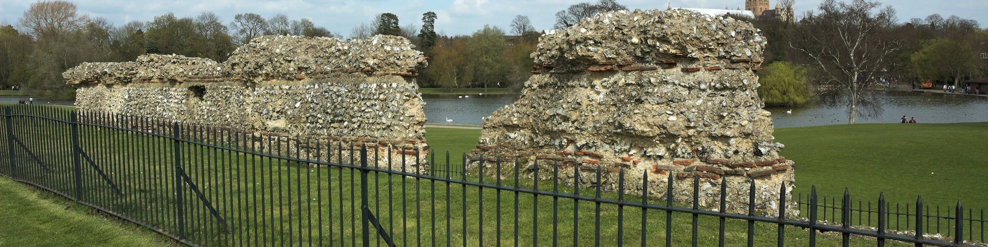Ruinas de piedra antiguas con un lago y una torre distante.