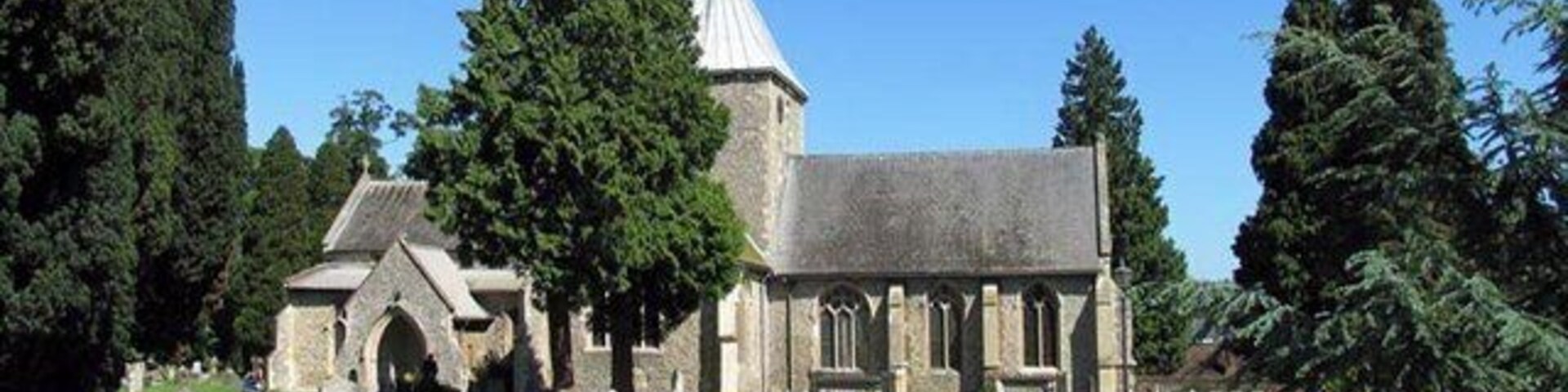 Una iglesia con un campanario alto, rodeada de lápidas y árboles.