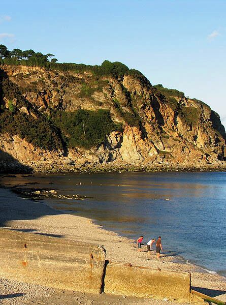 Una costa rocosa con una playa y gente caminando por la orilla.