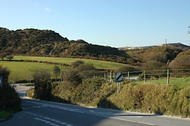 A rural road with a sharp bend, surrounded by green fields and hills.