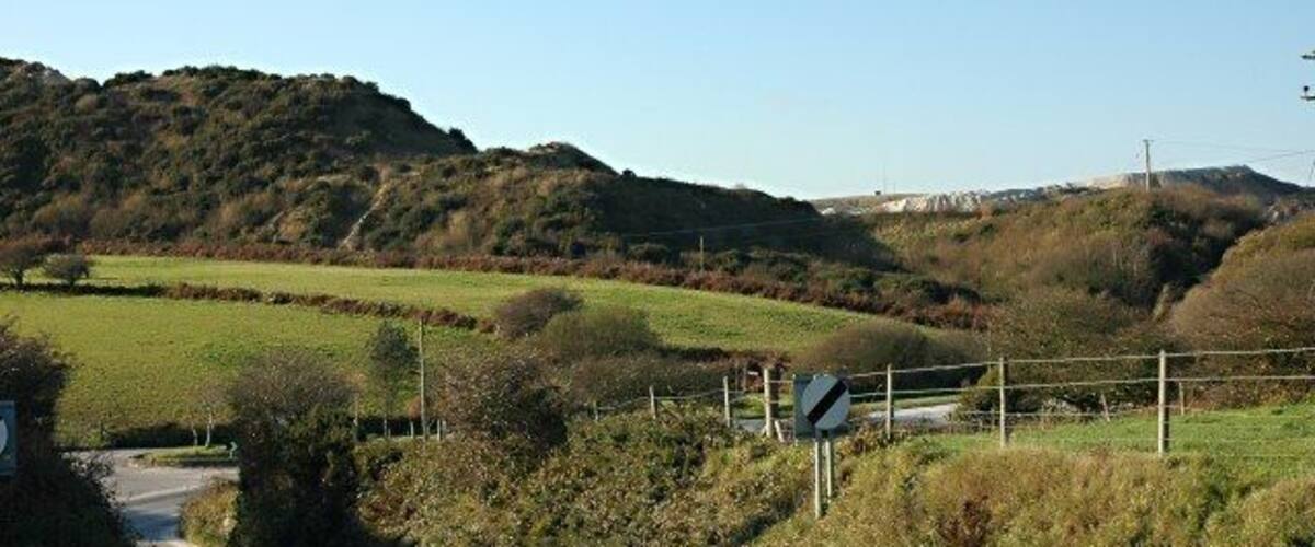 A rural road with a sharp bend, surrounded by green fields and hills.