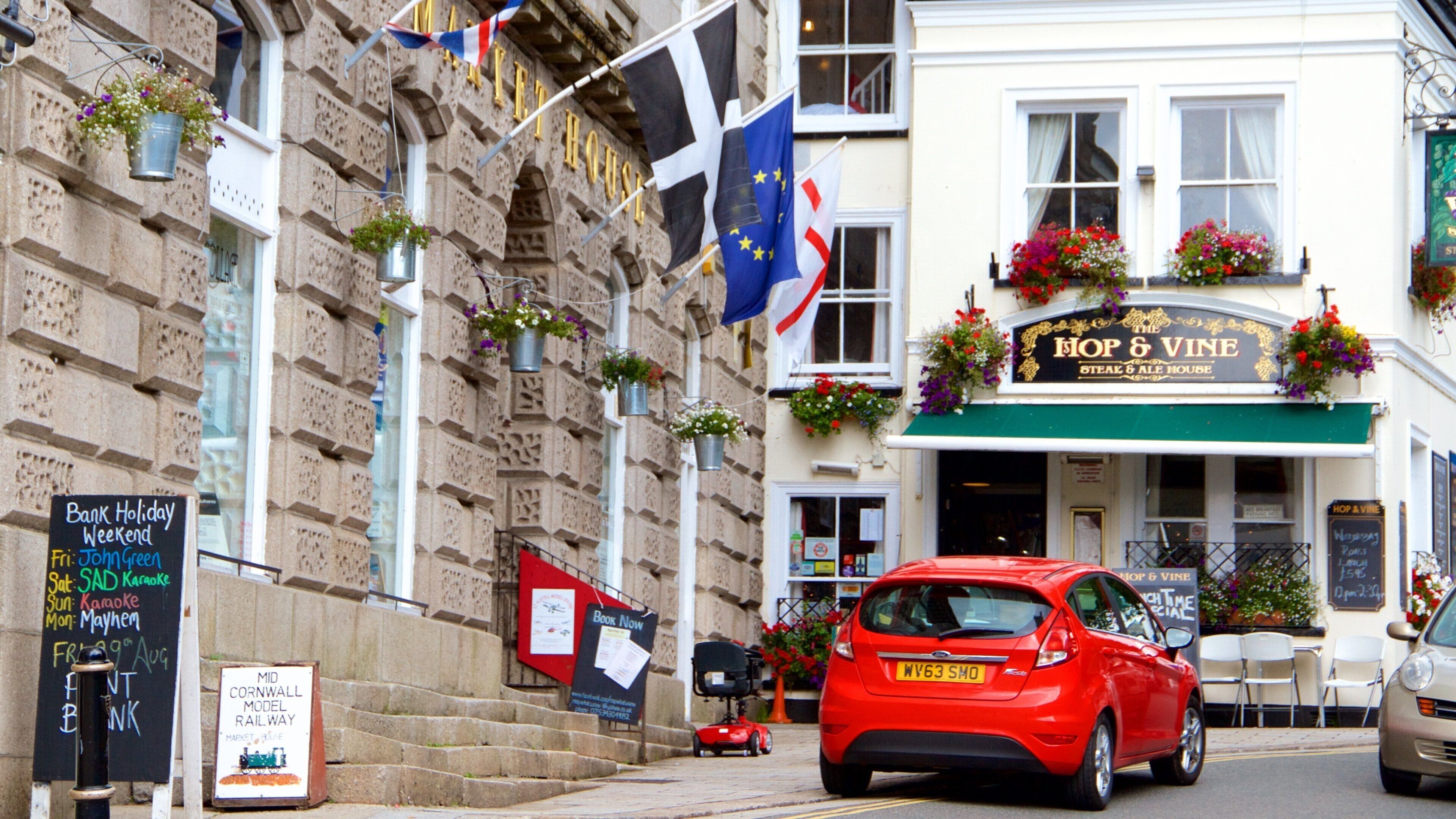 A red car parked in front of a pub named 'Hop & Vine'.