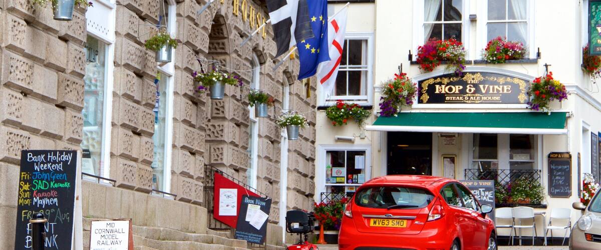 A red car parked in front of a pub named 'Hop & Vine'.