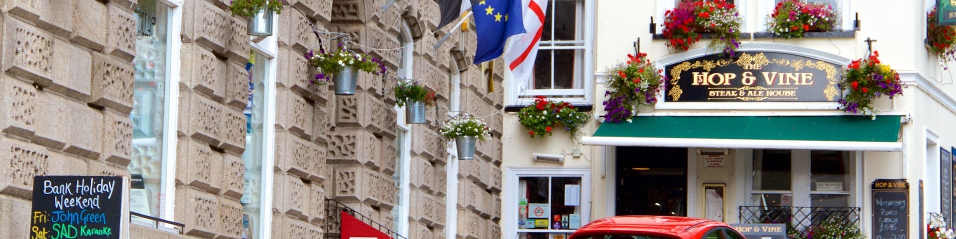A red car parked in front of a pub named 'Hop & Vine'.