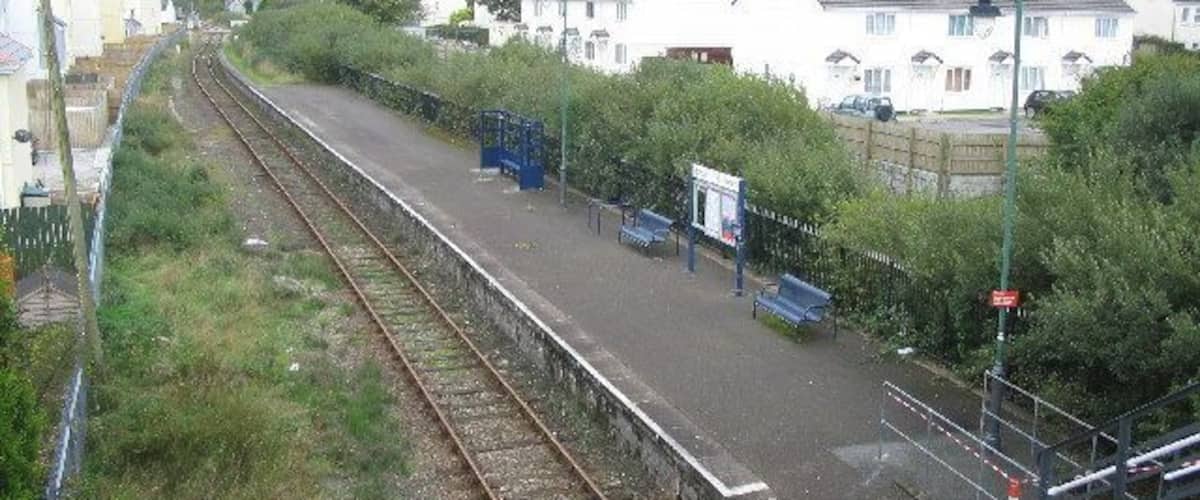 A railway station platform with tracks, benches, and a fence.