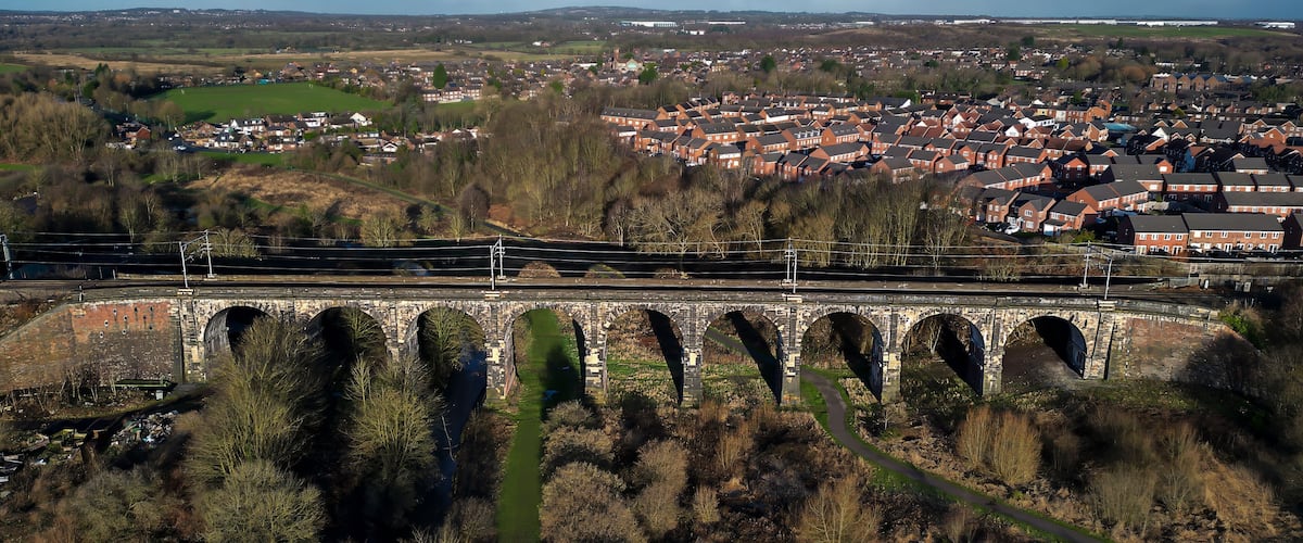 A railway bridge over a river, a town in the background, and surrounding hills.