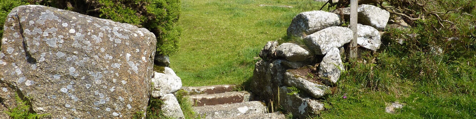 Un portón de piedra en un campo cubierto de hierba, con árboles y colinas al fondo.