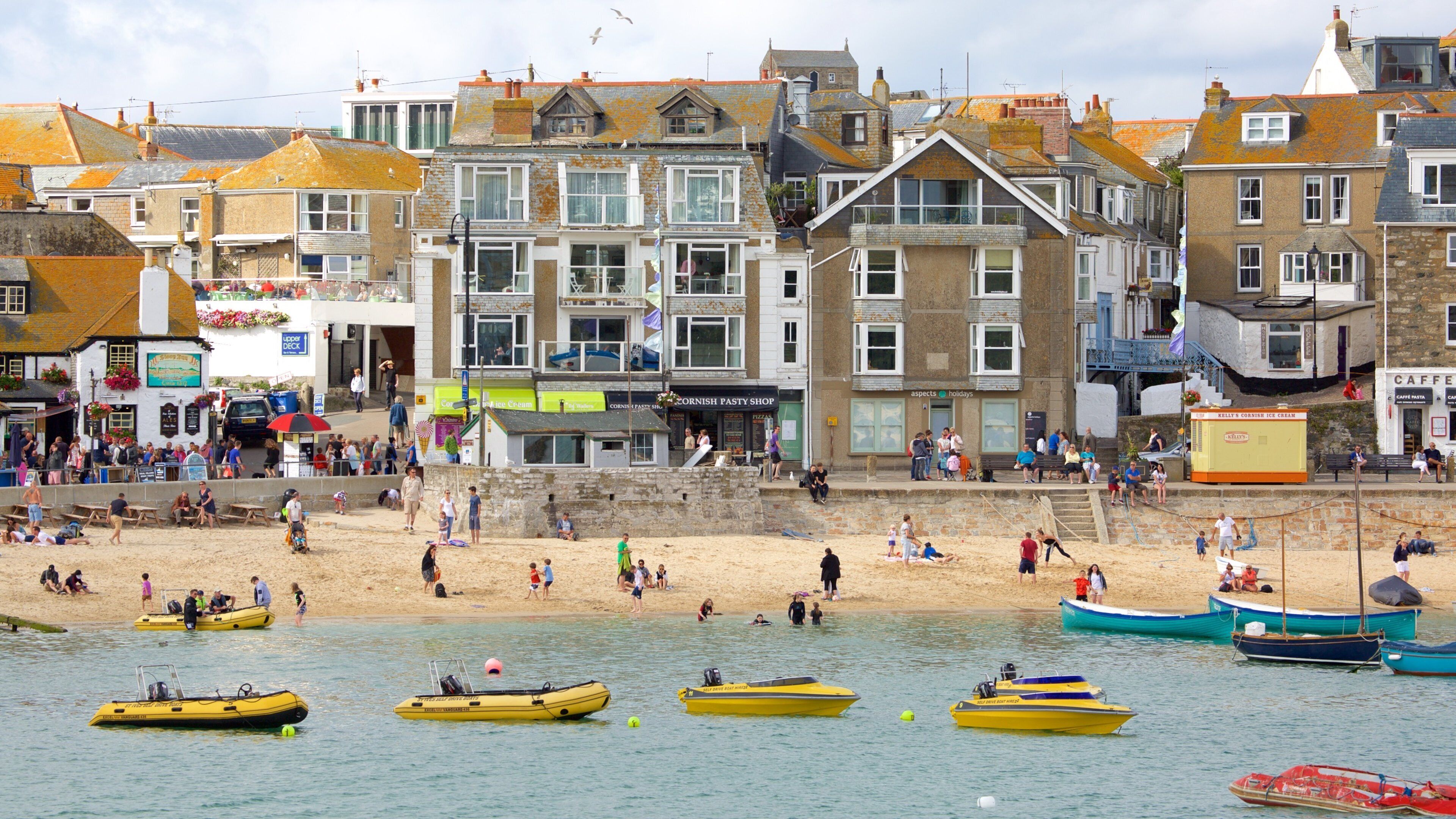 A beach with people, boats, and buildings in the background.