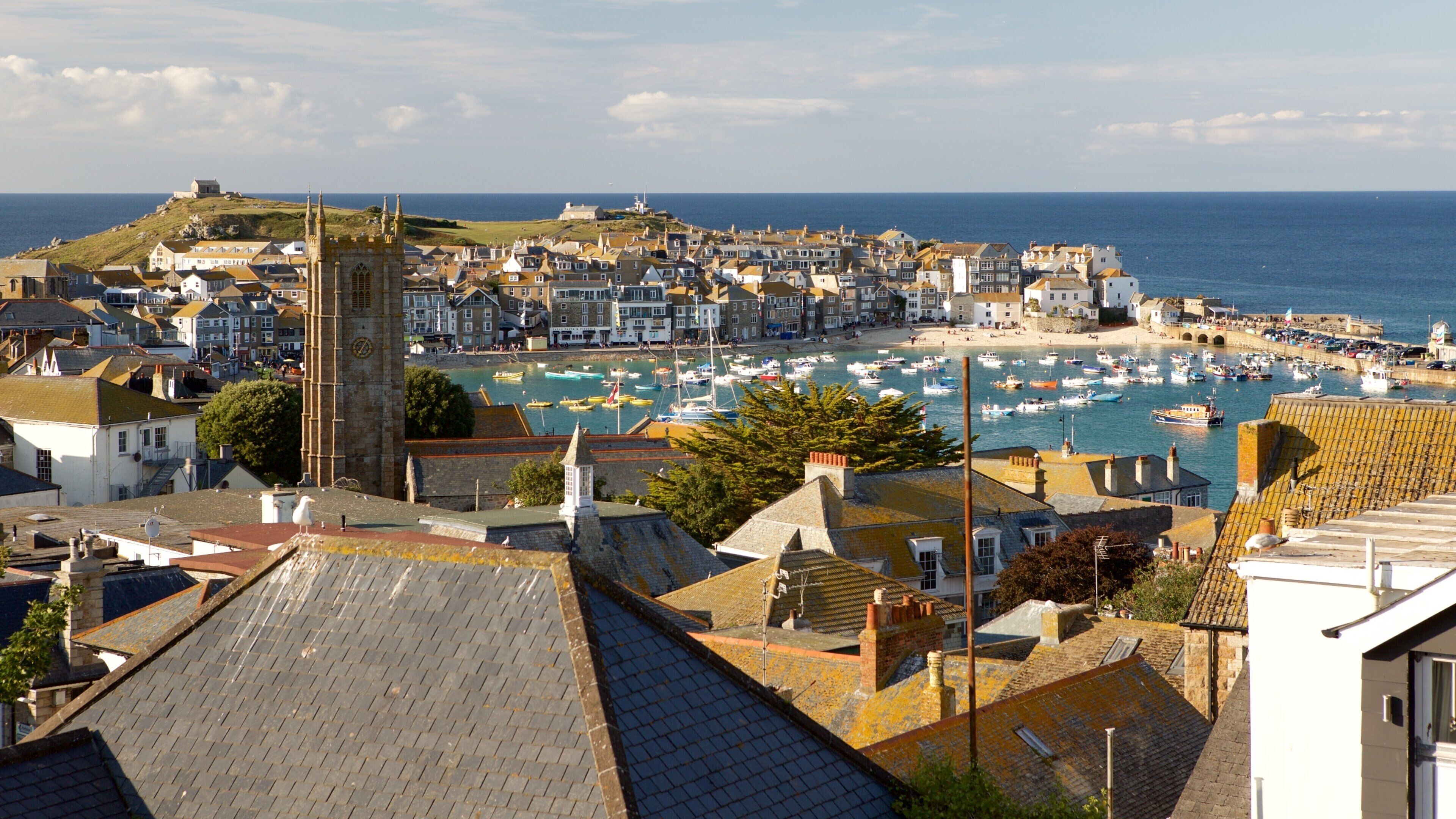 A coastal town with a prominent church tower, a harbor filled with boats, and a beach area.