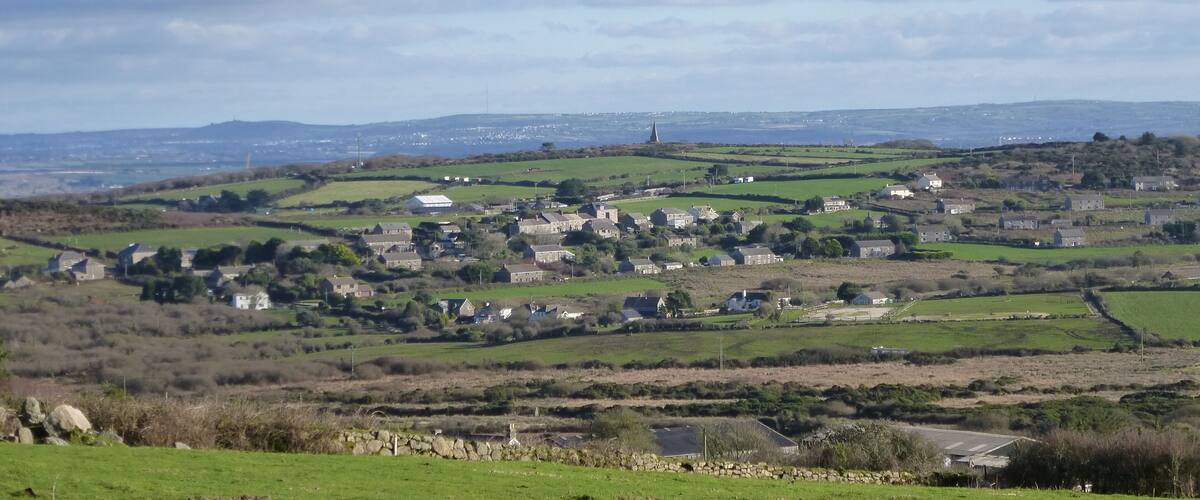 A rural landscape with rolling hills, scattered houses, and a distant church spire.