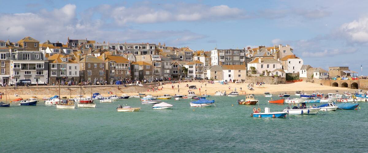 A coastal town with historic buildings, a sandy beach, and numerous boats in the water.