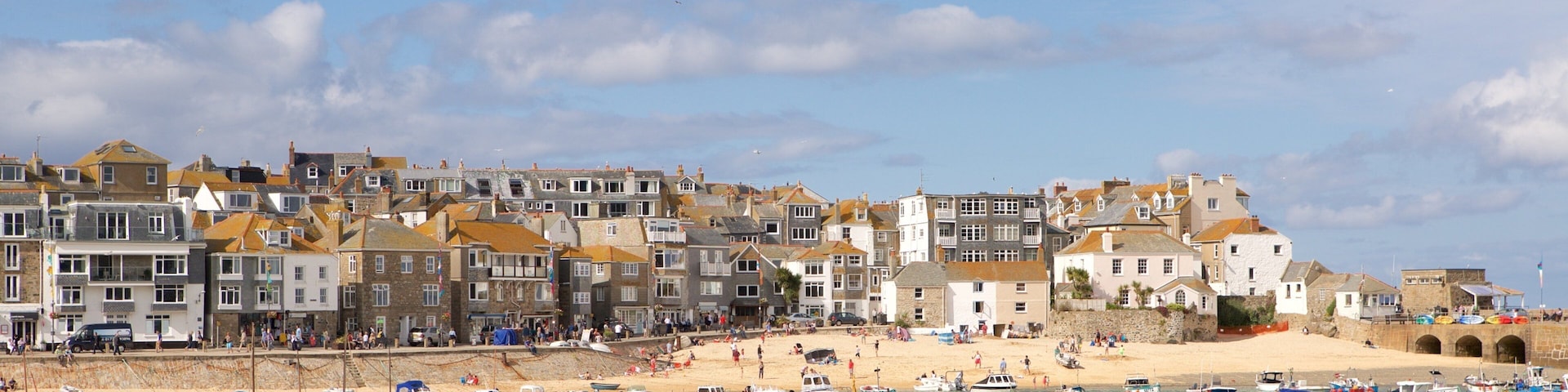 A coastal town with historic buildings, a sandy beach, and numerous boats in the water.