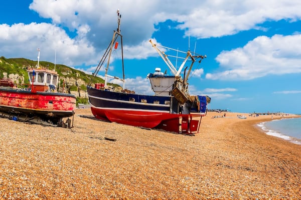 A pebbled beach with fishing boats, a lighthouse, and a coastal building.