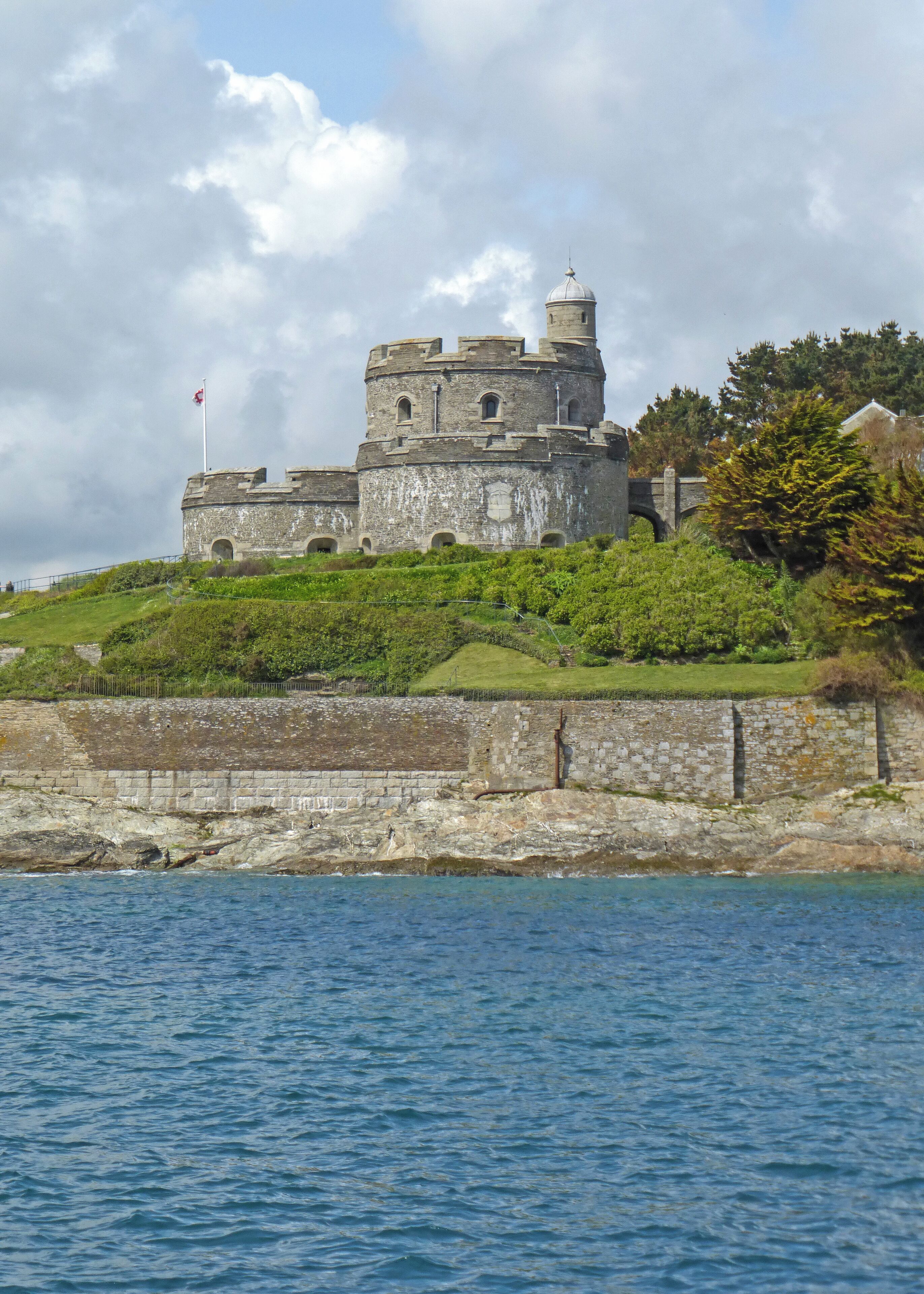 A historic stone castle on a grassy hill overlooking a body of water.