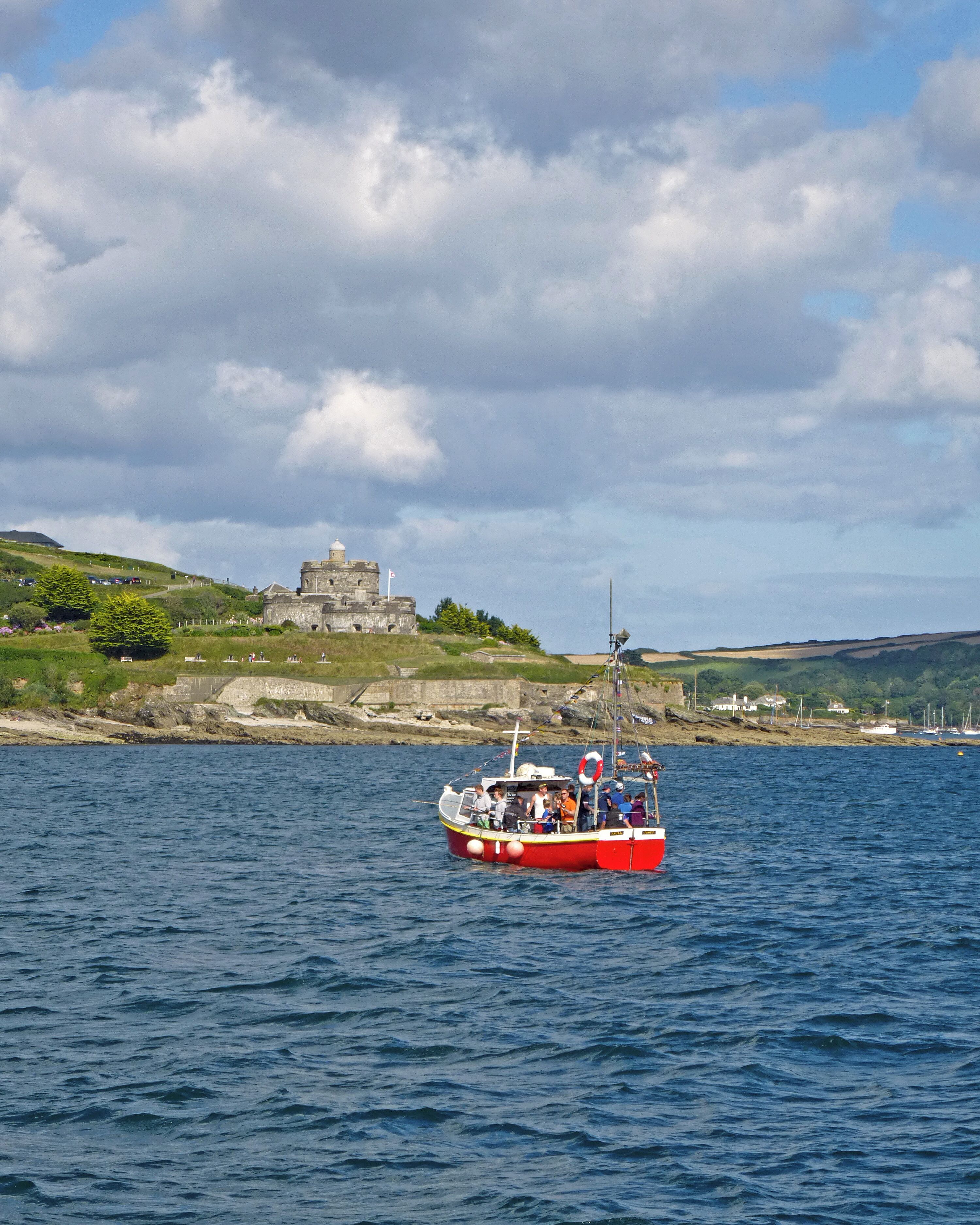 A red boat on calm waters with a historic building in the background.