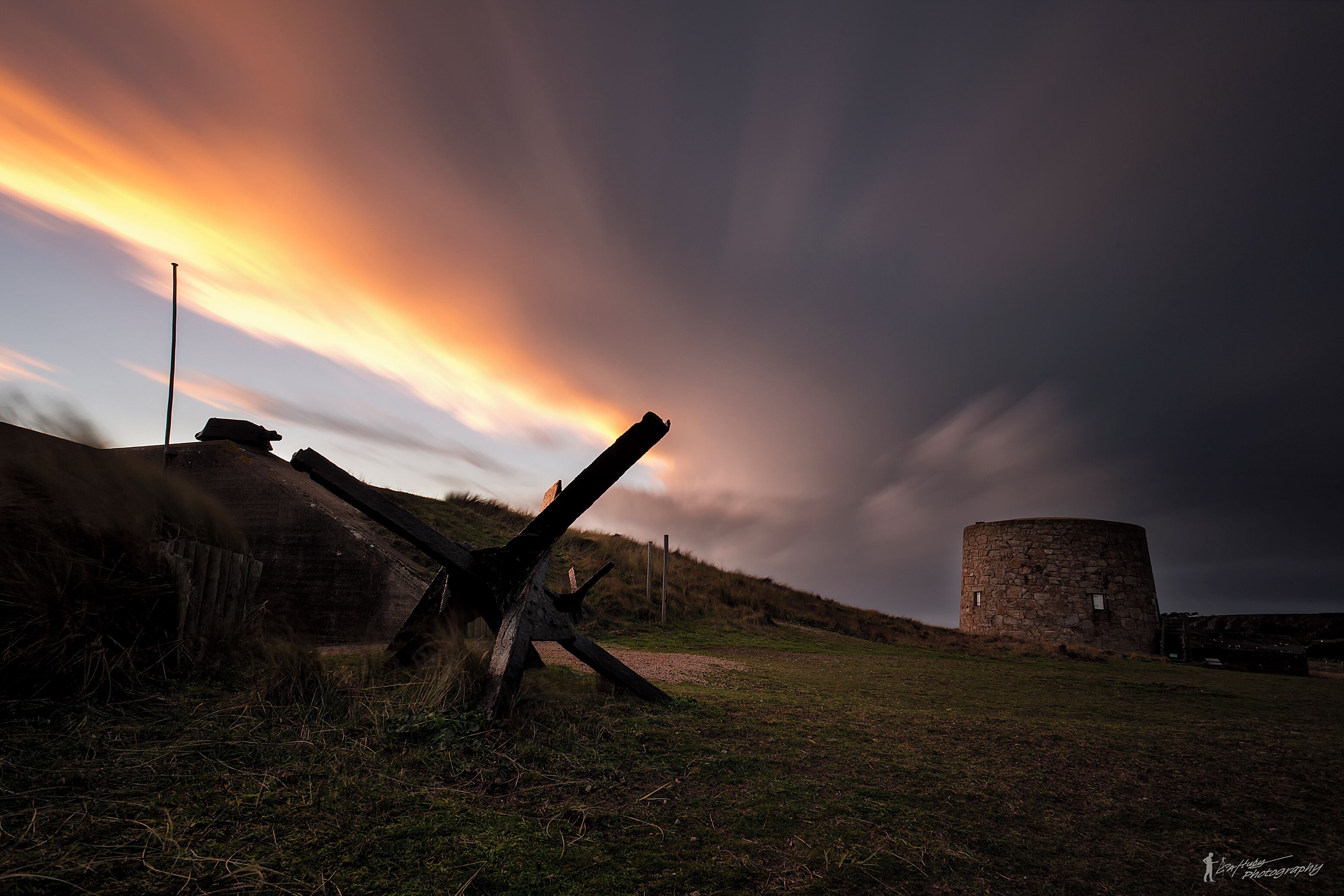 A stone tower on a grassy hill with a sunset in the background.
