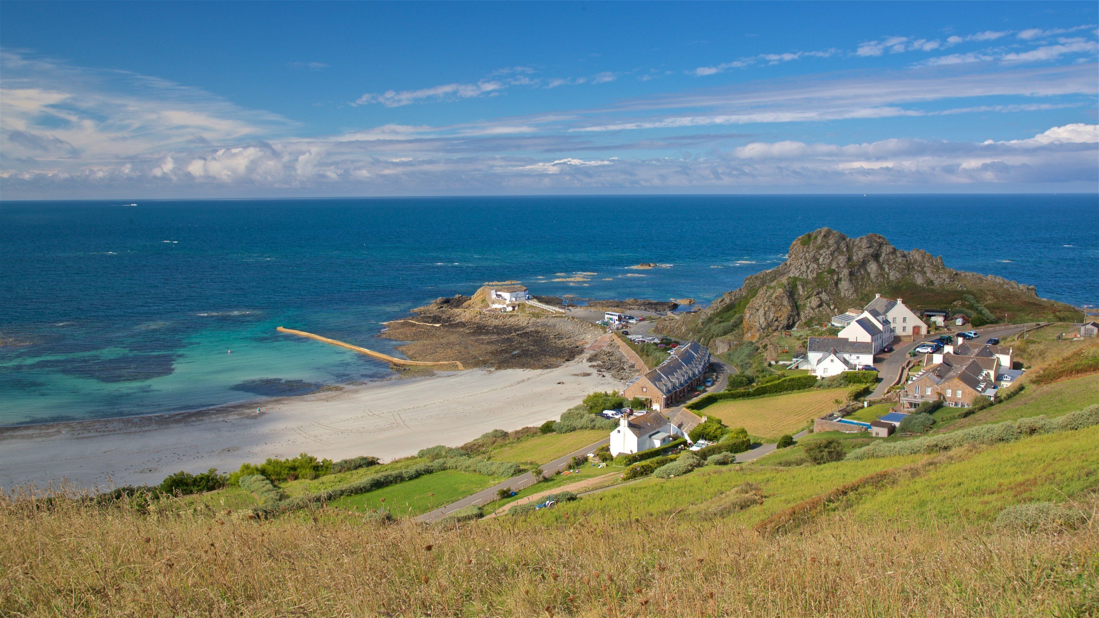 A coastal village with a rocky outcrop, sandy beach, and clear blue sea.