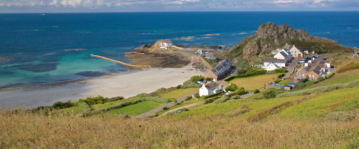 A coastal village with a rocky outcrop, sandy beach, and clear blue sea.
