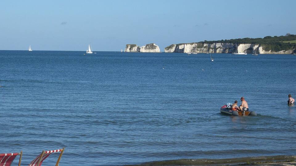 A beach with a sandy shore, a few beach chairs, and a calm sea with boats in the distance.