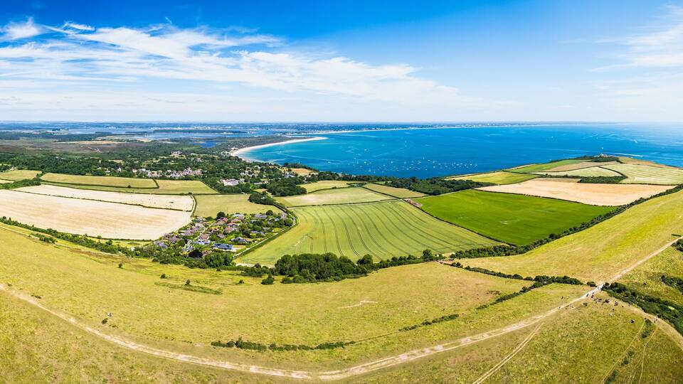 An aerial view of a coastal landscape with fields, a small village, and a curving coastline.