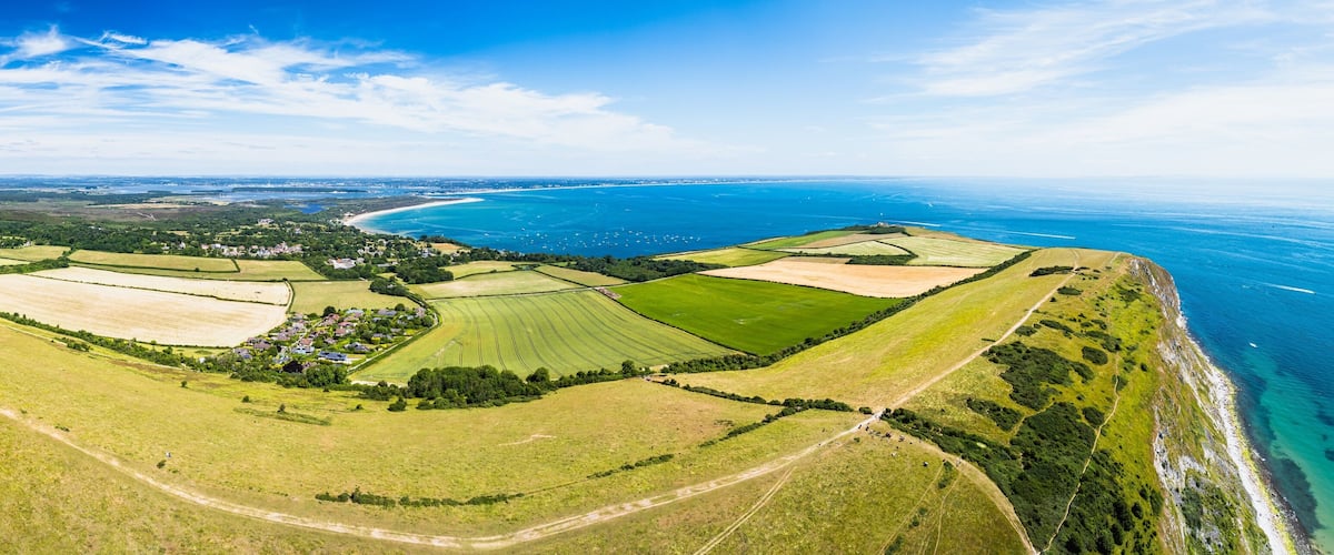An aerial view of a coastal landscape with fields, a small village, and a curving coastline.