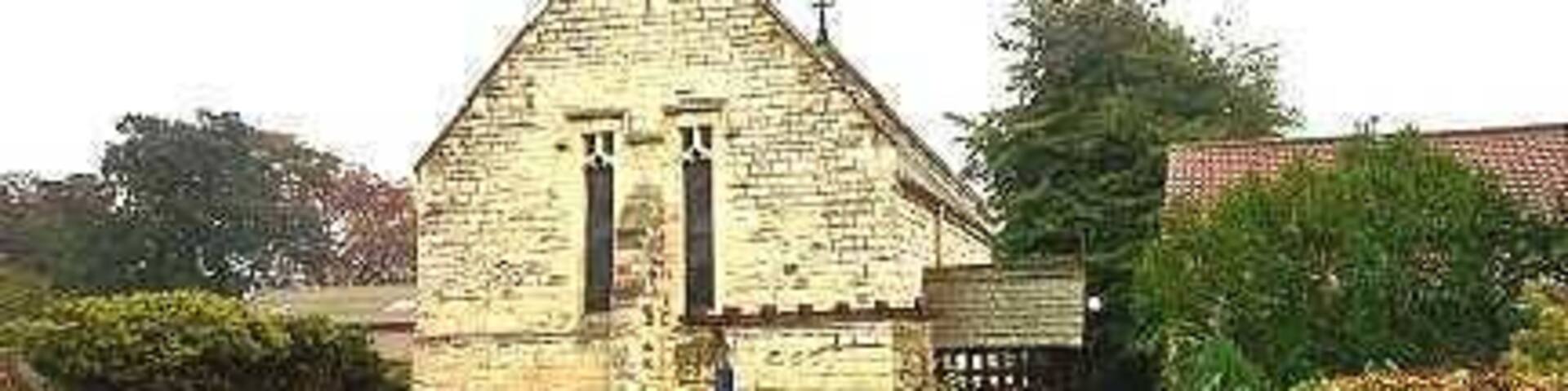 A stone church with a bell tower, surrounded by greenery and a brick wall.