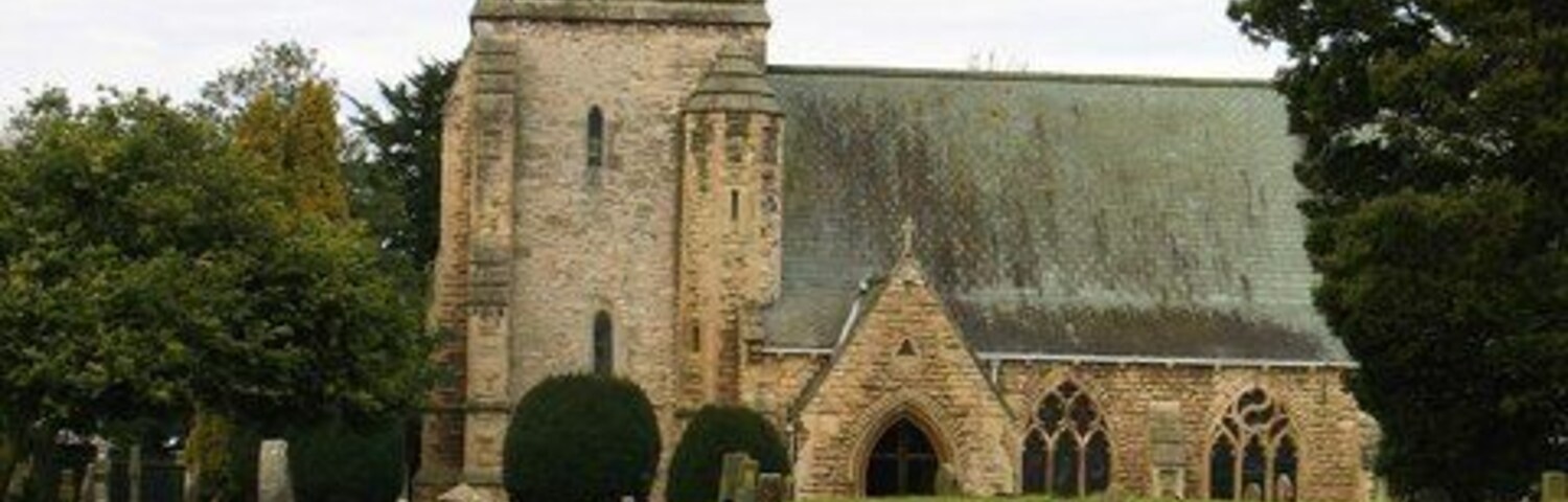 Nave and west tower of St John the Baptist's parish church, Kirkby Wharfe, North Yorkshire, seen from the south. It is February and snowdrops are blooming in the churchyard.