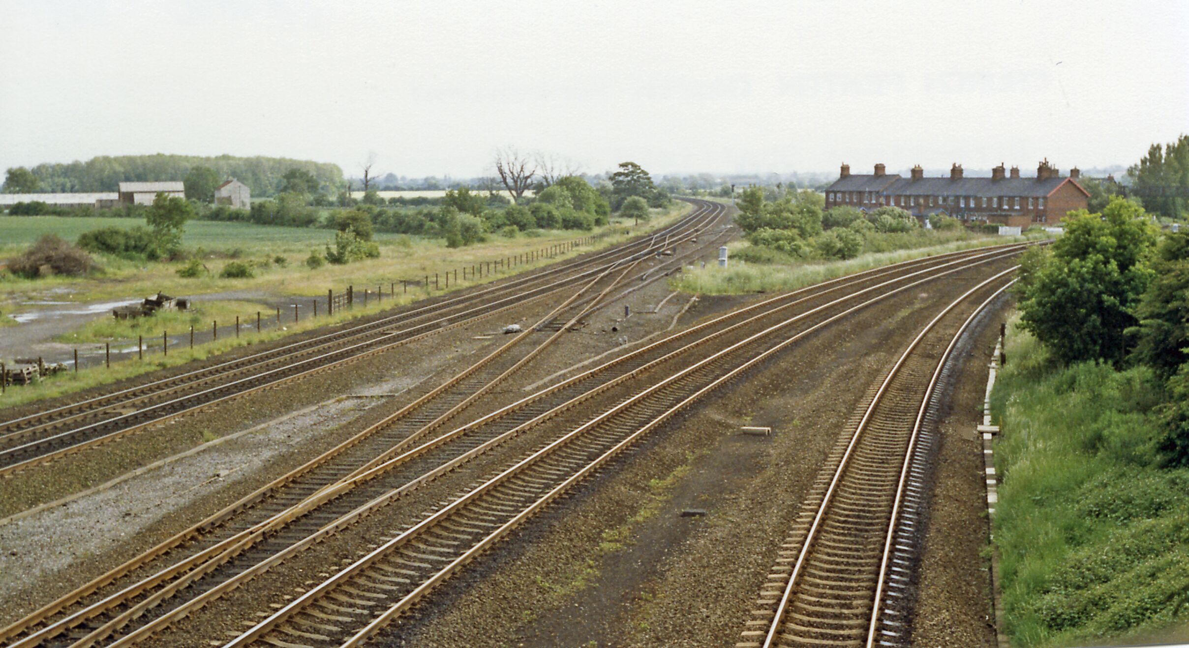 A railway track layout with multiple tracks converging and diverging, surrounded by greenery and buildings.