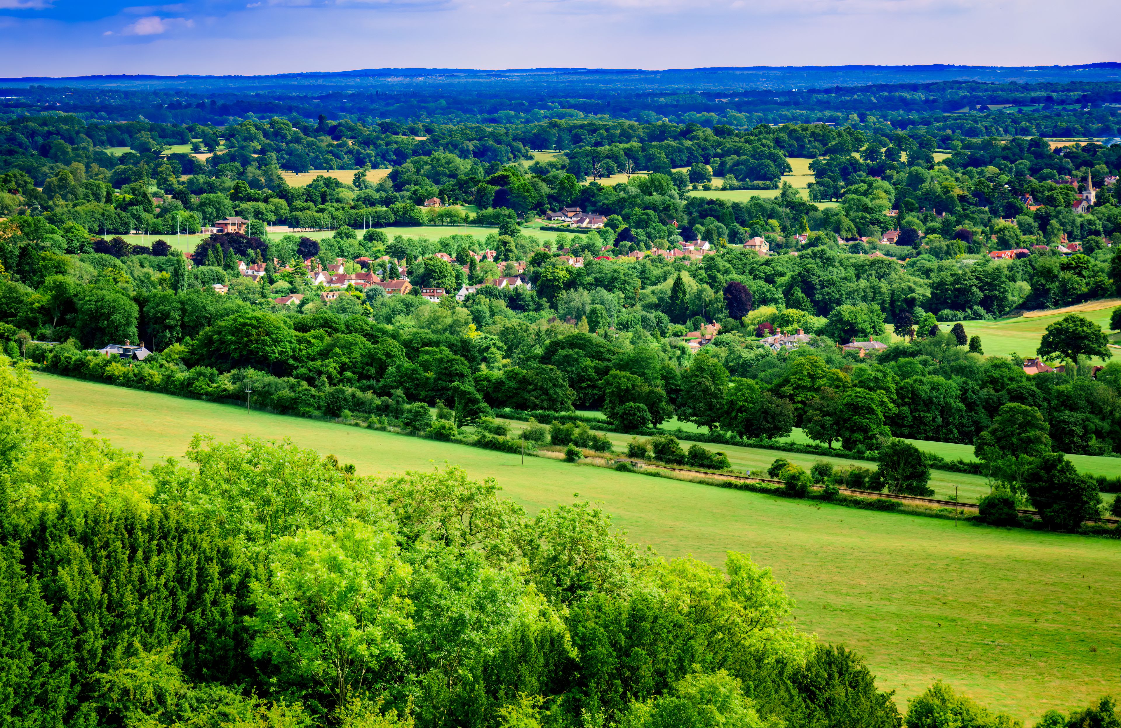 A lush green landscape with rolling hills, scattered houses, and dense tree coverage.