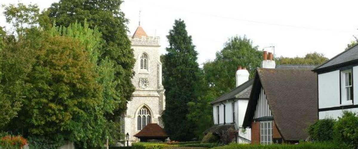 A pathway leading to a church with a tower, surrounded by well-maintained hedges and a traditional house.
