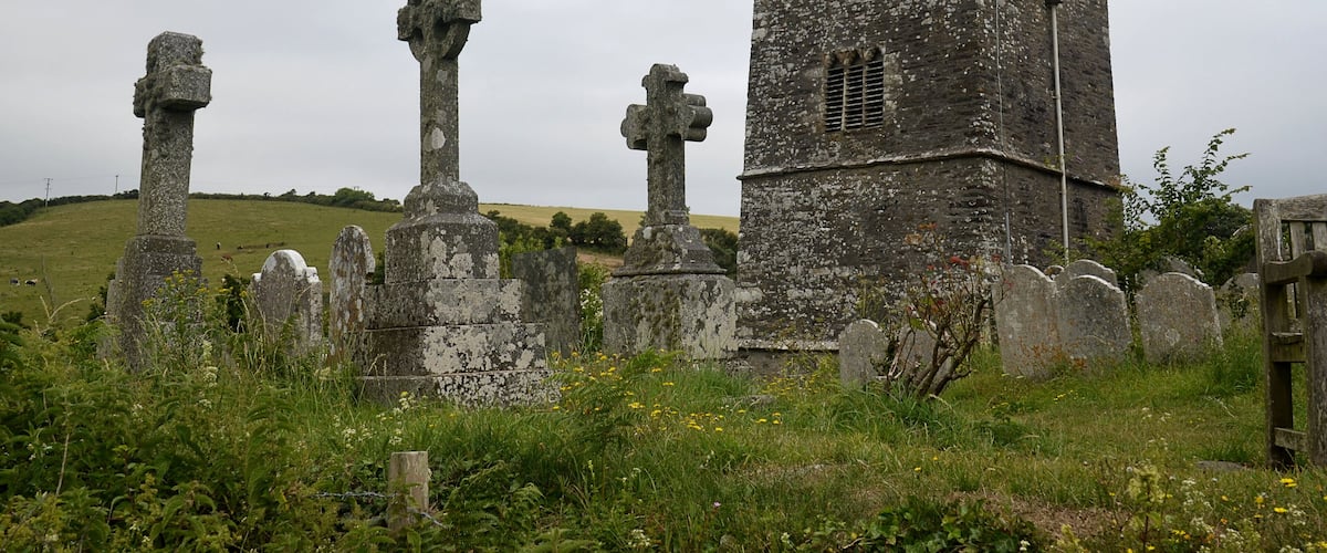 A historic tower with a cross at its peak, surrounded by ancient stone crosses and a grassy field.