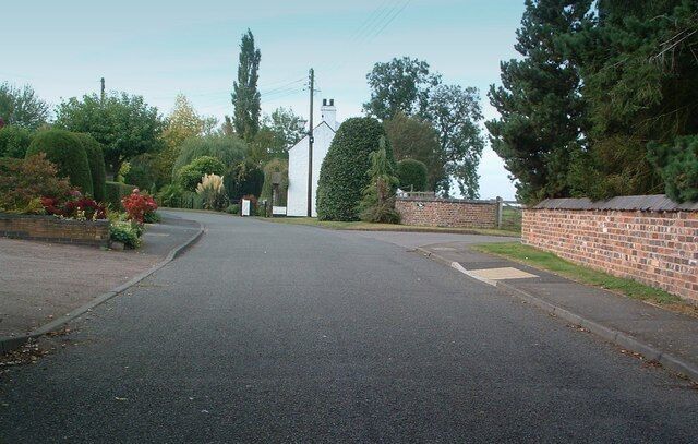 A quiet residential street with a white church, brick walls, and lush greenery.
