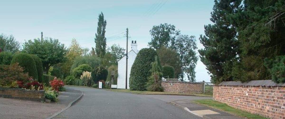 A quiet residential street with a white church, brick walls, and lush greenery.