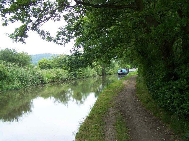 A narrow waterway flanked by dense greenery, a path, and a distant vehicle.