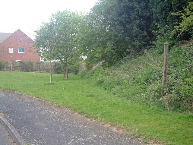 A rural road with a grassy verge, a red brick house, and a wooden post with 'PUBLIC ROAD' written on it.