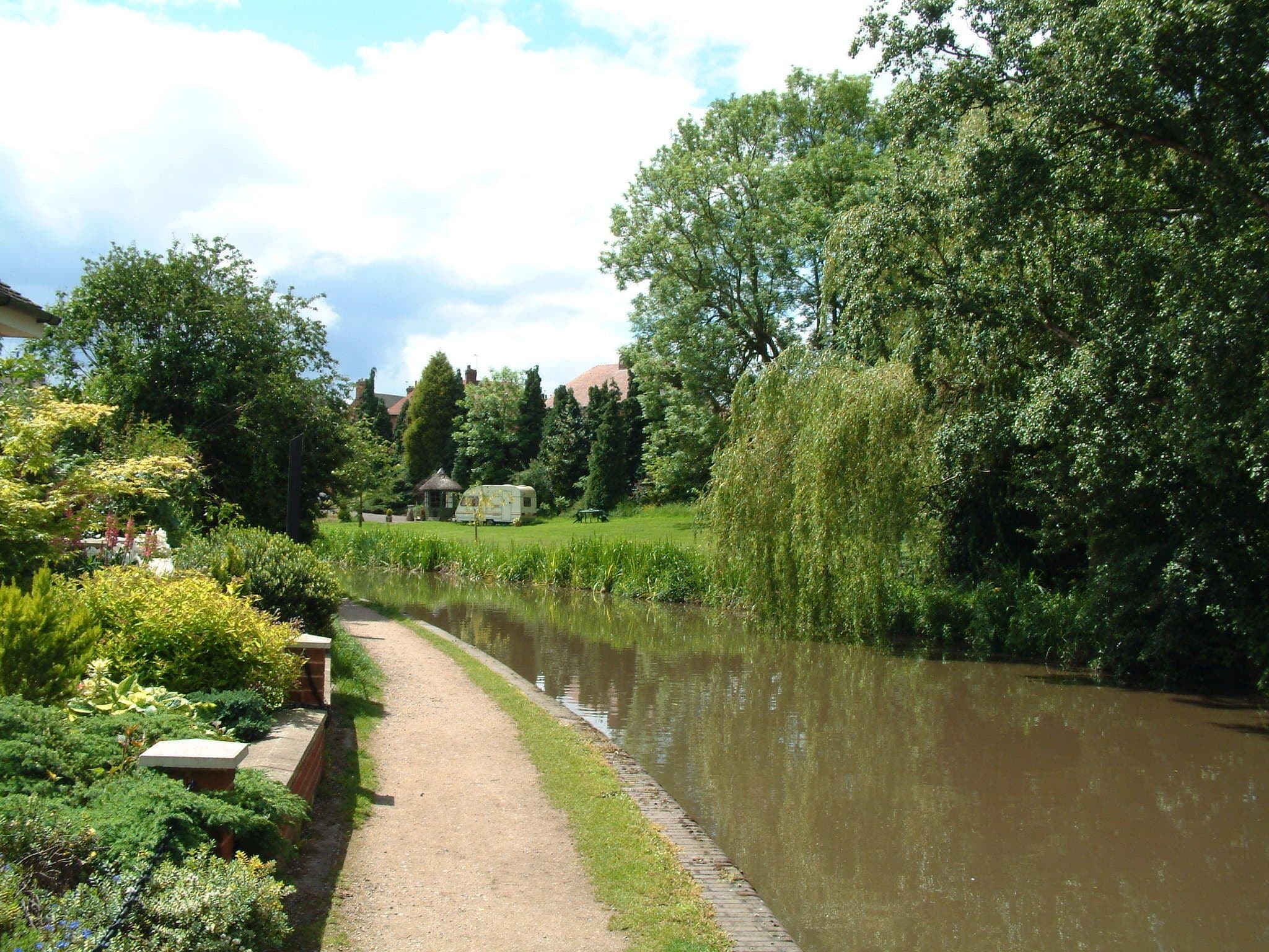 A riverside path with lush greenery and a white RV parked by the water.