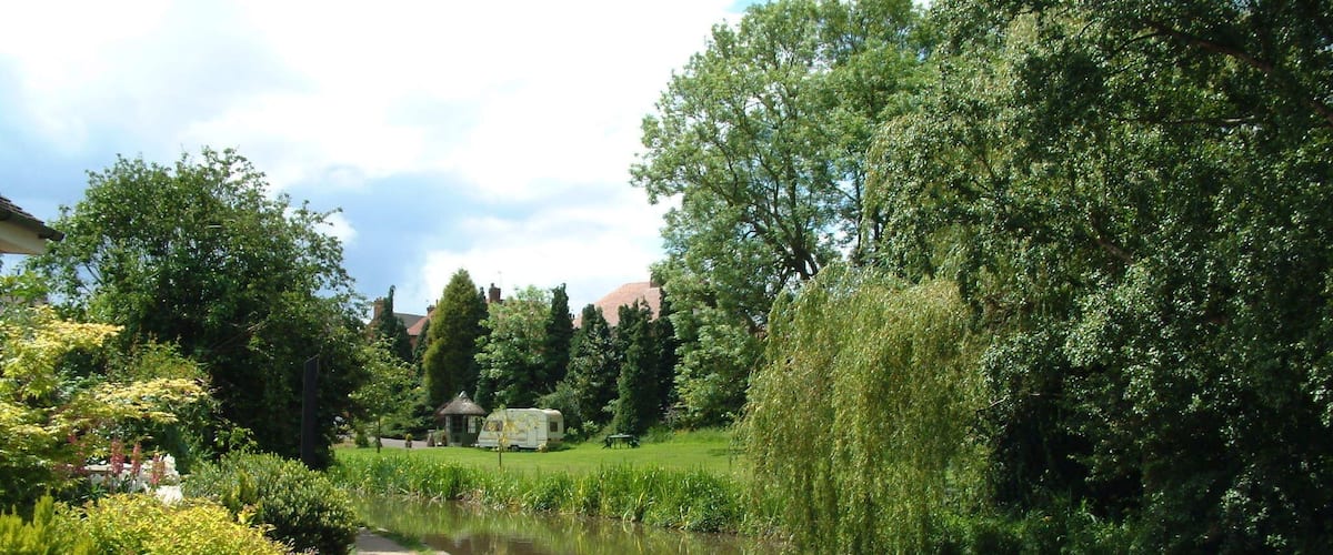 A riverside path with lush greenery and a white RV parked by the water.