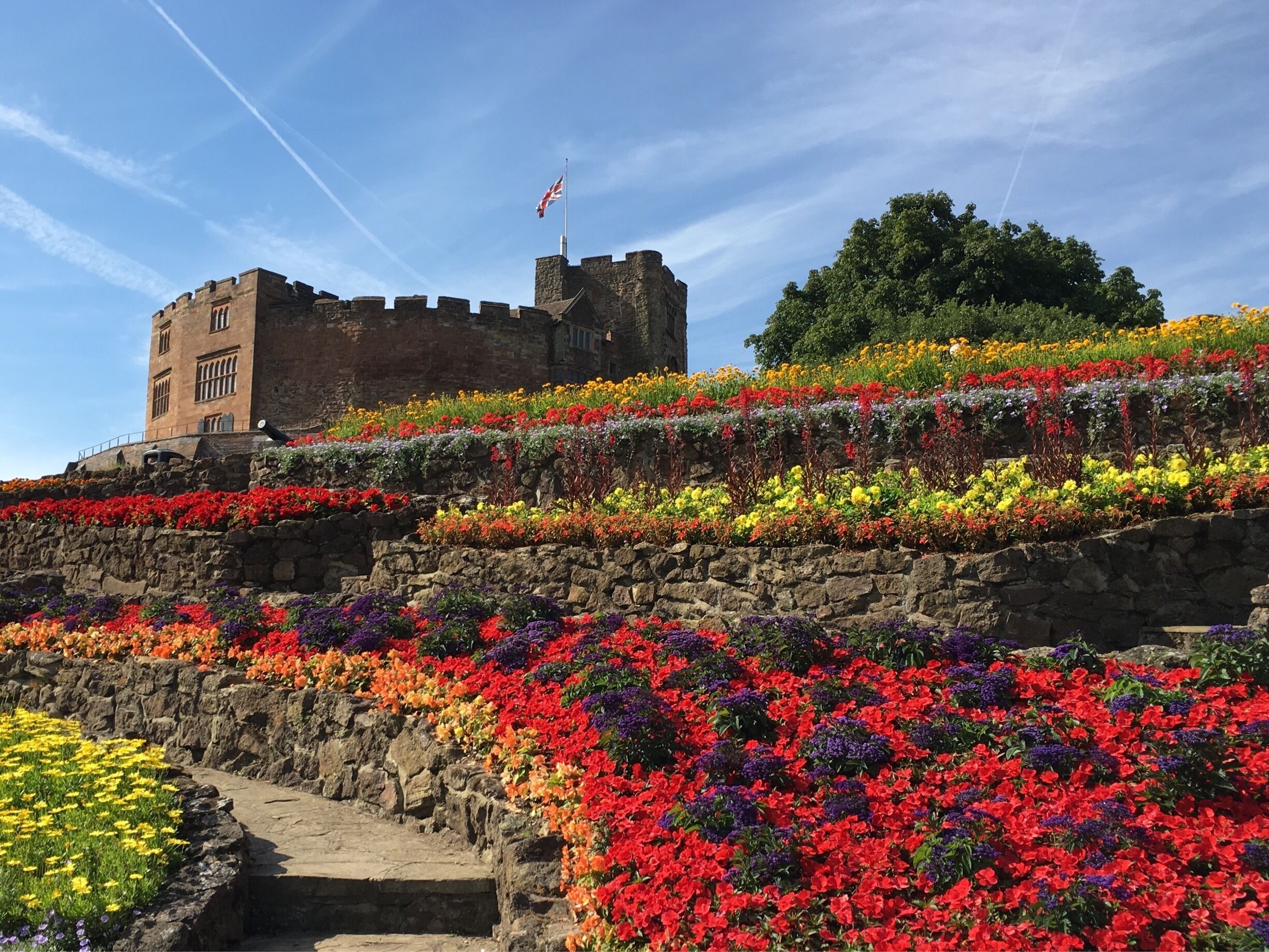 A castle with a flag, surrounded by colorful flower beds.
