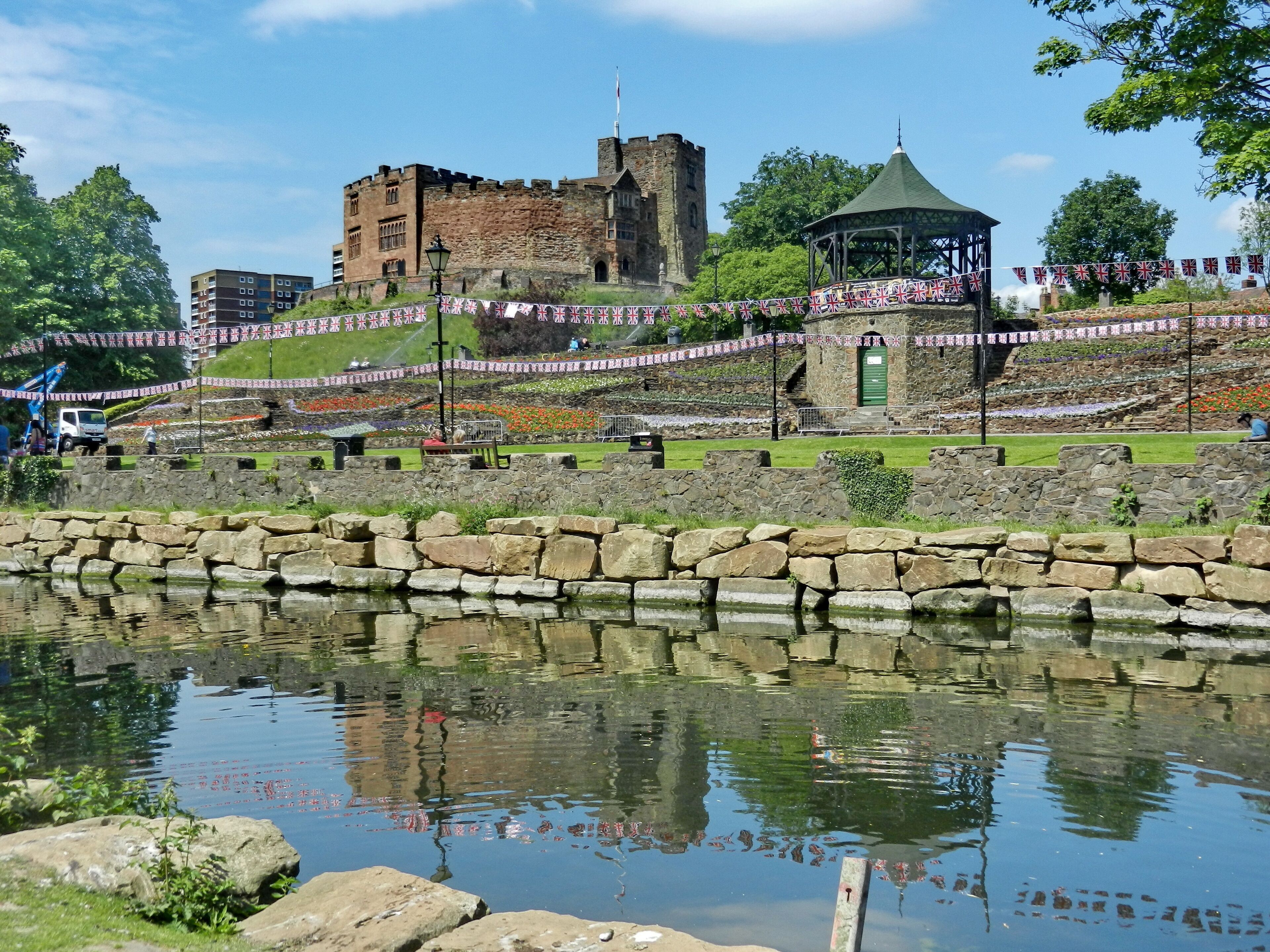 A castle, a gazebo, and a stone wall with a pond in the foreground.