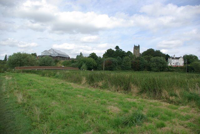 A grassy field with a bridge, a castle-like structure, and a large white building in the background.