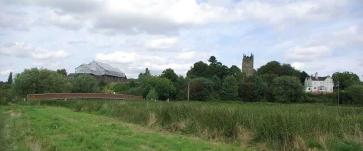 A grassy field with a bridge, a castle-like structure, and a large white building in the background.