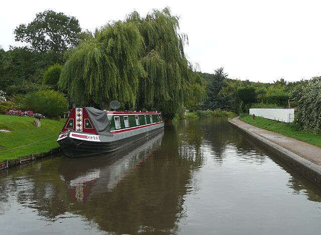 A narrowboat docked by a weeping willow tree on a calm river.