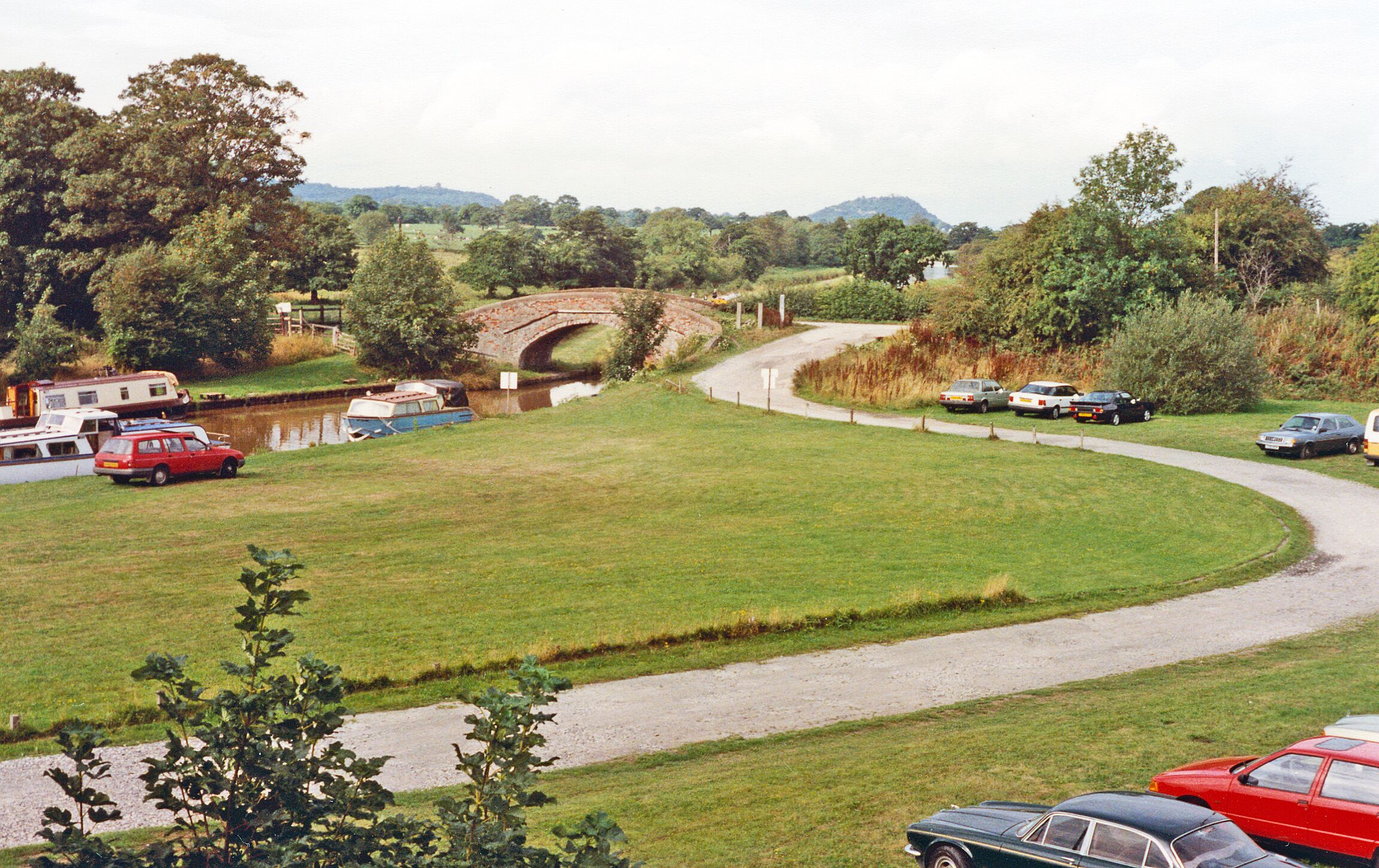 A rural landscape with a winding road, a bridge, and parked cars.