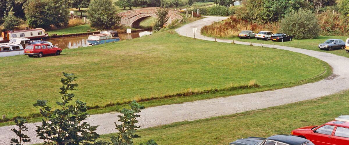 A rural landscape with a winding road, a bridge, and parked cars.