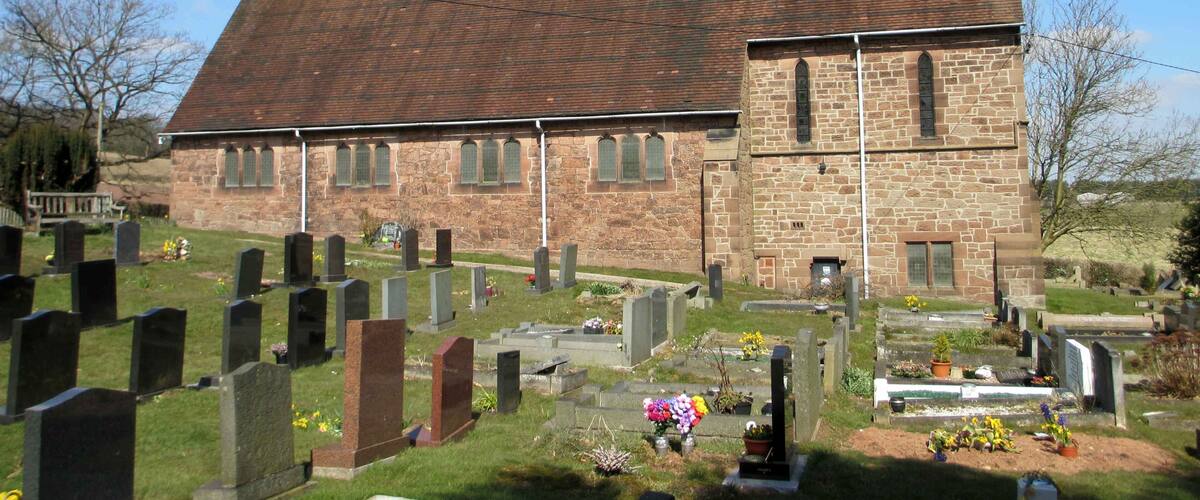 A church with a red-tiled roof and stone walls, surrounded by a cemetery with gravestones and flowers.