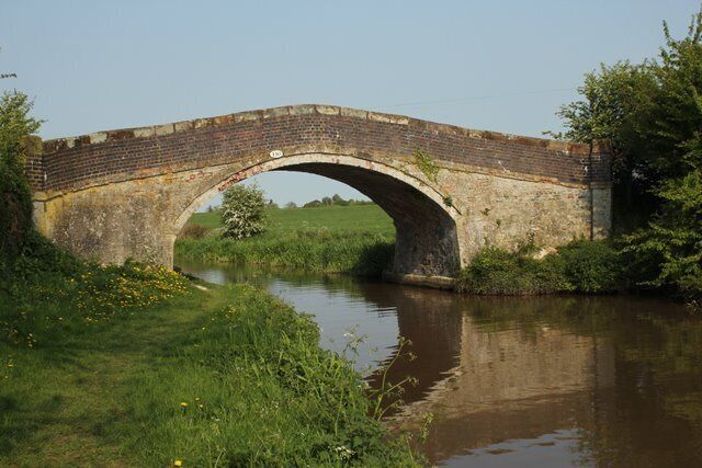 A stone bridge over a calm river, surrounded by greenery.