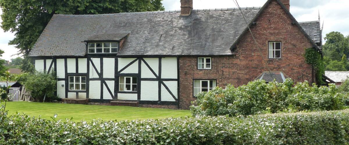 A Tudor-style house with a white and black timber frame, brick walls, and a grey tiled roof.