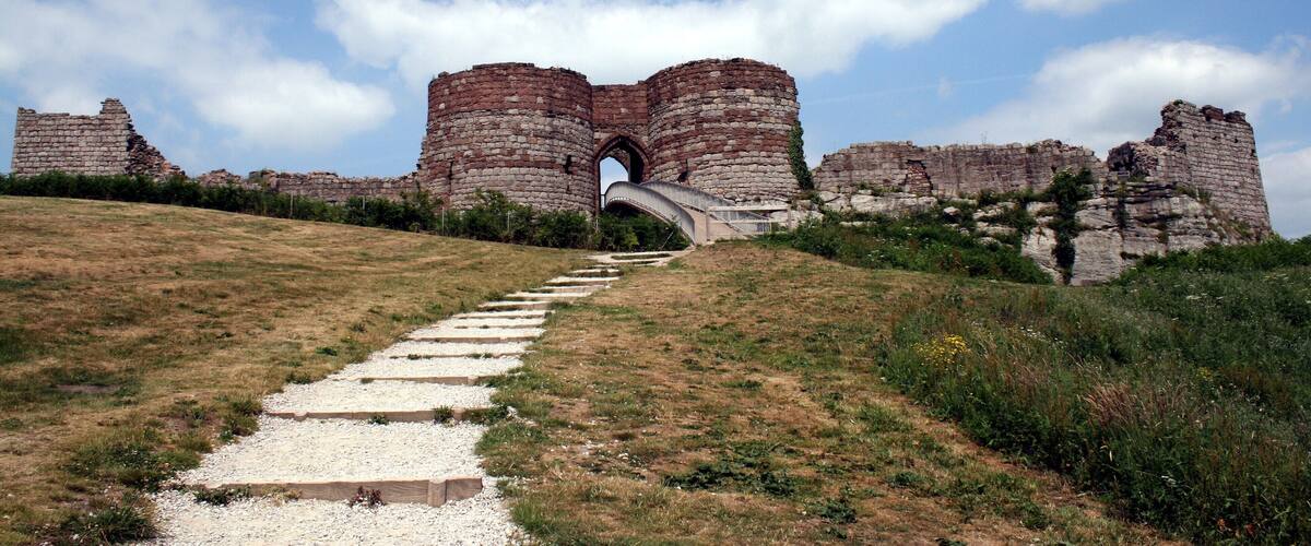 A historical stone archway leading to a large brick castle on a grassy hill.