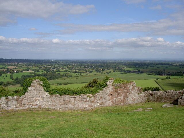 Un muro de piedra y ruinas en un campo cubierto de hierba, con vistas a campos verdes y un cielo nublado.