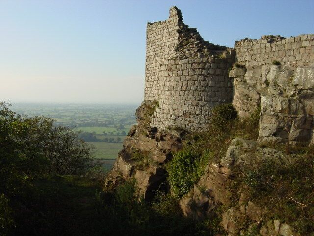 A ruined stone tower on a hillside overlooking a valley.